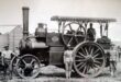 Black and white photo of men posing beside a vintage steam engine, showcasing early 20th-century transportation technology.