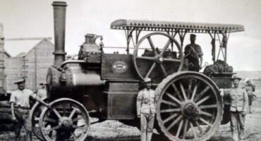 Black and white photo of men posing beside a vintage steam engine, showcasing early 20th-century transportation technology.