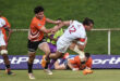 Rugby player in an orange and black jersey sprinting while holding a ball, showcasing athleticism and determination.