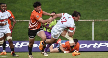 Rugby player in an orange and black jersey sprinting while holding a ball, showcasing athleticism and determination.