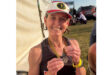 A woman smiles while holding a medal, showcasing her achievement and joy.