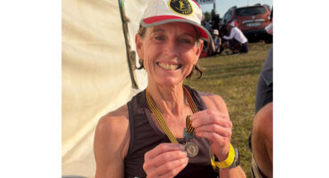 A woman smiles while holding a medal, showcasing her achievement and joy.