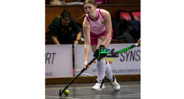 A woman in a pink uniform skillfully playing field hockey.