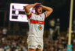 A rugby player stands on the field with his hands on his head, expressing frustration or disbelief during a game.