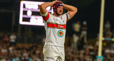 A rugby player stands on the field with his hands on his head, expressing frustration or disbelief during a game.