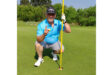 A man in golf attire kneels on the grass, focused on a golf ball on the course.