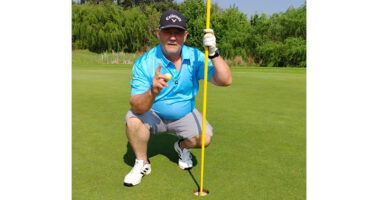 A man in golf attire kneels on the grass, focused on a golf ball on the course.