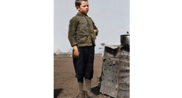 A boy stands beside a large pile of bricks, looking up with curiosity and interest.