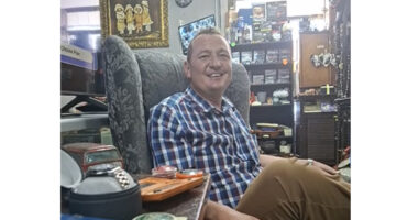 A man in a chair, showcasing a wristwatch, exudes a calm and thoughtful demeanor.