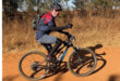 A man cycling on a dirt road surrounded by greenery and trees.