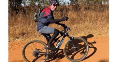 A man cycling on a dirt road surrounded by greenery and trees.