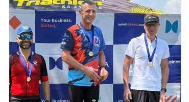 Three men stand on a podium, each wearing medals; one man proudly holds his medal aloft.