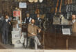 A group of men stands in a store, with one man in the center, engaged in conversation or discussion.