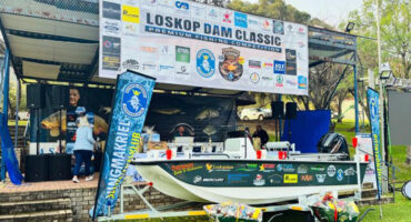 A boat is docked in front of a tent displaying a sign, indicating the location or event taking place.