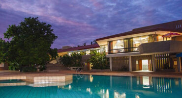 A serene pool illuminated by dusk light, situated in front of a modern building with a tranquil atmosphere.