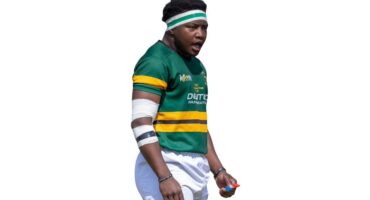 A man wearing a green and yellow jersey holds a rugby ball, preparing for a play on the field.