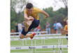 A young boy leaps over a hurdle during a race, showcasing determination and athleticism.