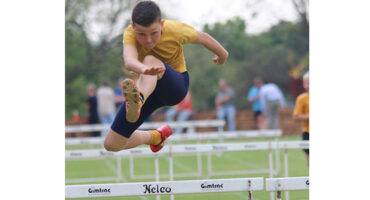 A young boy leaps over a hurdle during a race, showcasing determination and athleticism.