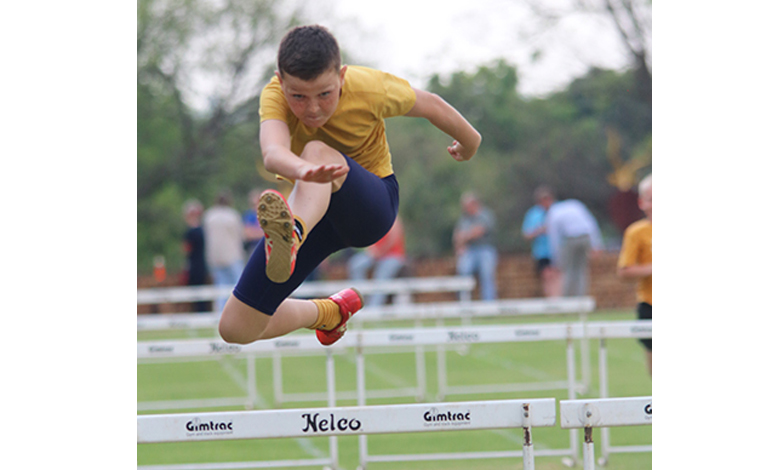 A young boy leaps over a hurdle during a race, showcasing determination and athleticism.
