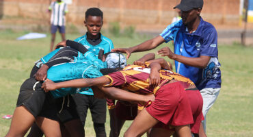 A group of young men engaged in a rugby match on a grassy field, showcasing teamwork and athleticism.