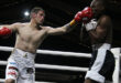 Two boxers in a ring, one wearing red gloves, engaged in an intense match.
