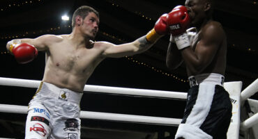 Two boxers in a ring, one wearing red gloves, engaged in an intense match.
