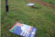 A campaign sign lies on the grass, featuring bold text and graphics related to an election.
