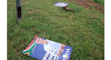 A campaign sign lies on the grass, featuring bold text and graphics related to an election.