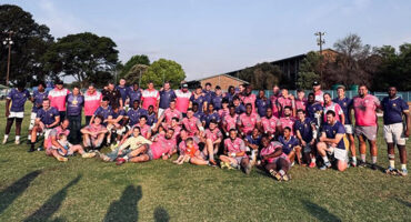 A group of individuals wearing matching pink shirts and pants, standing together in a cheerful pose.