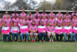 A rugby team in pink shirts poses together on the field, showcasing team spirit and unity.