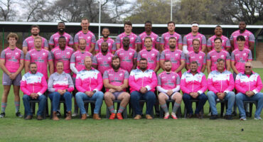 A rugby team in pink shirts poses together on the field, showcasing team spirit and unity.