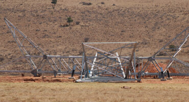 A towering metal structure is situated in a vast field, surrounded by greenery and open space.