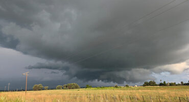 A dark storm cloud looms over a vast green field, indicating an impending downpour.