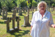 A woman gazes thoughtfully at a cross in a cemetery, surrounded by gravestones, evoking a sense of loss and remembrance.