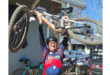 A man stands outside, lifting his bike with both hands, showcasing its features and design.