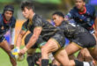 A rugby player sprinting down the field, gripping the ball tightly as he prepares to evade defenders.