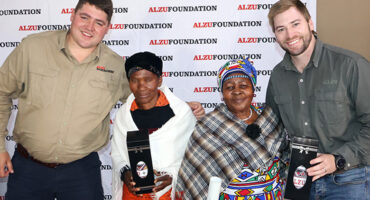 Four individuals proudly display their awards while smiling joyfully at the camera.