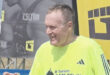 A man in a yellow shirt is speaking to an unseen individual, conveying a friendly demeanor.