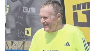 A man in a yellow shirt is speaking to an unseen individual, conveying a friendly demeanor.
