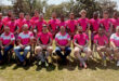 Several rugby players dressed in matching pink shirts and white pants, posing together in a relaxed environment.