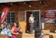 A diverse crowd of people gathered outside a large building, engaged in conversation and looking towards the entrance.