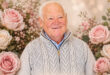 A man wearing a sweater is surrounded by blooming pink roses, highlighting a peaceful and floral setting.