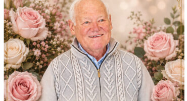 A man wearing a sweater is surrounded by blooming pink roses, highlighting a peaceful and floral setting.