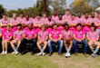 A group of men wearing matching pink shirts and shorts, standing together outdoors, smiling at the camera.
