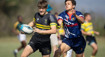 Two young men engage in a rugby match on a grassy field, showcasing athleticism and teamwork.
