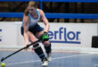 A woman in athletic gear skillfully playing field hockey on a court, focused on the ball and her teammates.