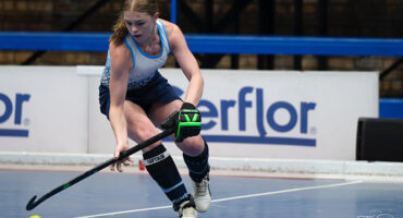 A woman in athletic gear skillfully playing field hockey on a court, focused on the ball and her teammates.