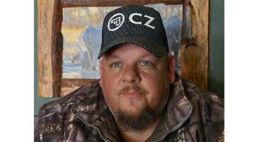 A man dons a camouflage jacket and hat, presenting a blend of style and practicality for outdoor environments.