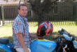 A man wearing a helmet sits on a blue motorcycle, ready for a ride.