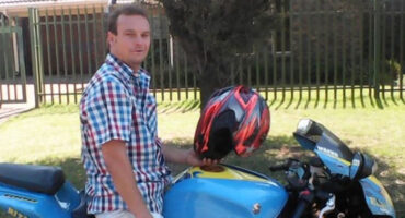 A man wearing a helmet sits on a blue motorcycle, ready for a ride.